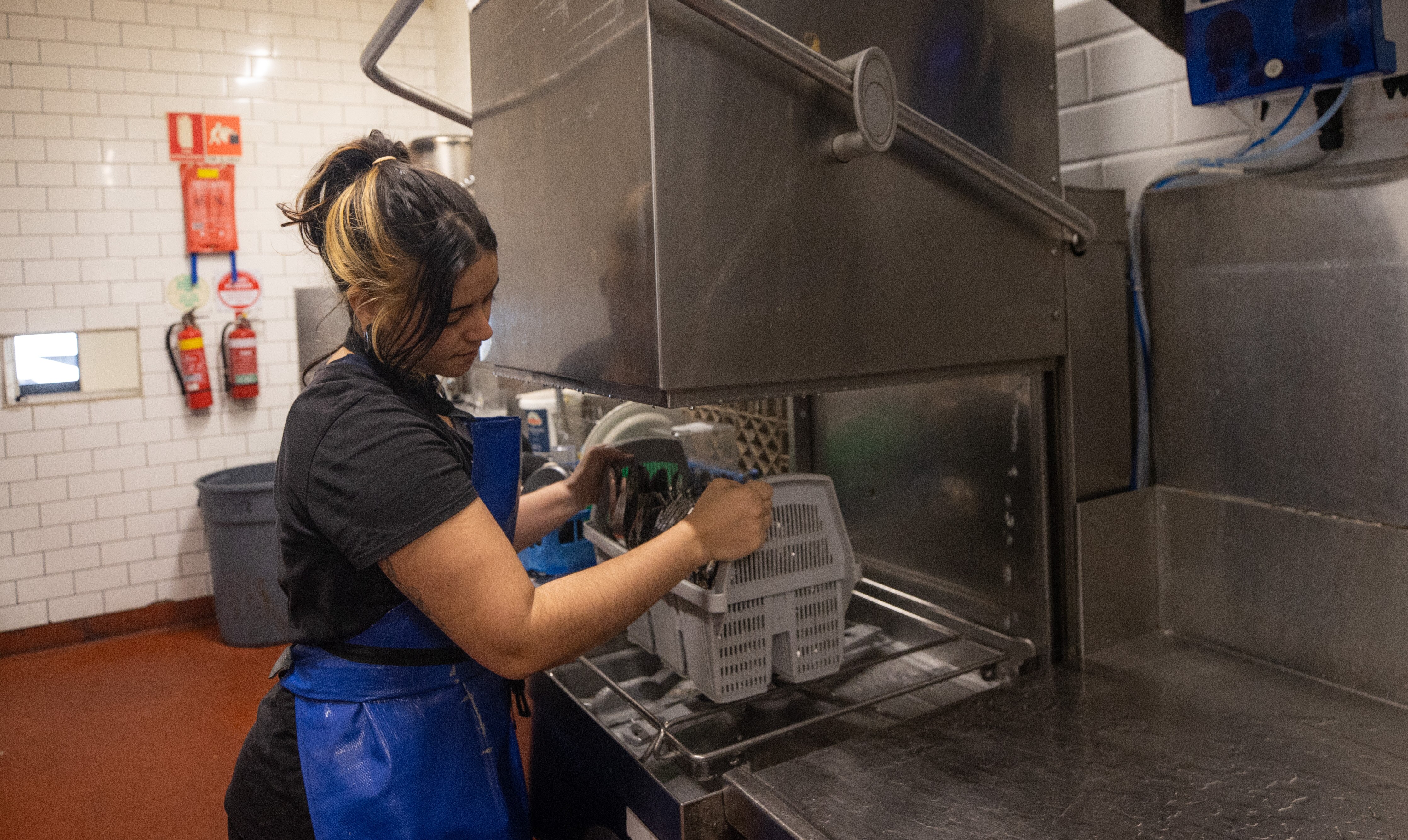 Woman with hair tied back packs an industrial dishwasher in a kitchen.