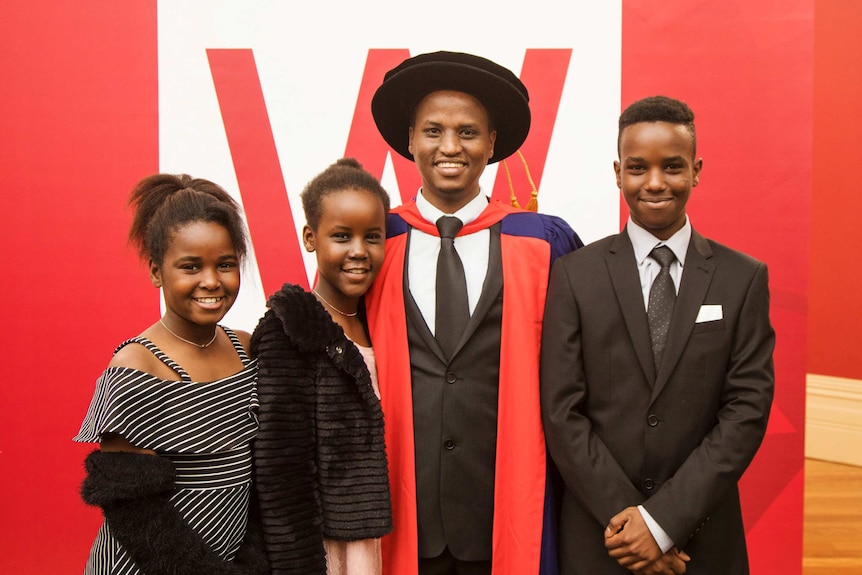 A smiling family flanks a man in a graduation outfit.