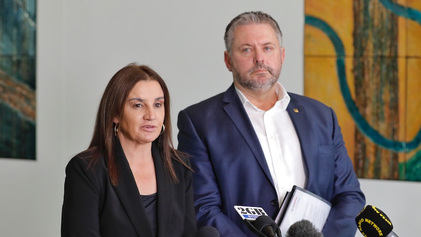 Jacqui Lambie and Glenn Kolomeitz stand in front of microphones at a press conference inside Parliament House