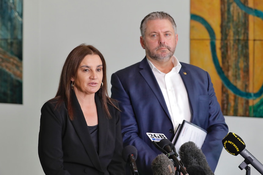 Jacqui Lambie and Glenn Kolomeitz stand in front of microphones at a press conference inside Parliament House