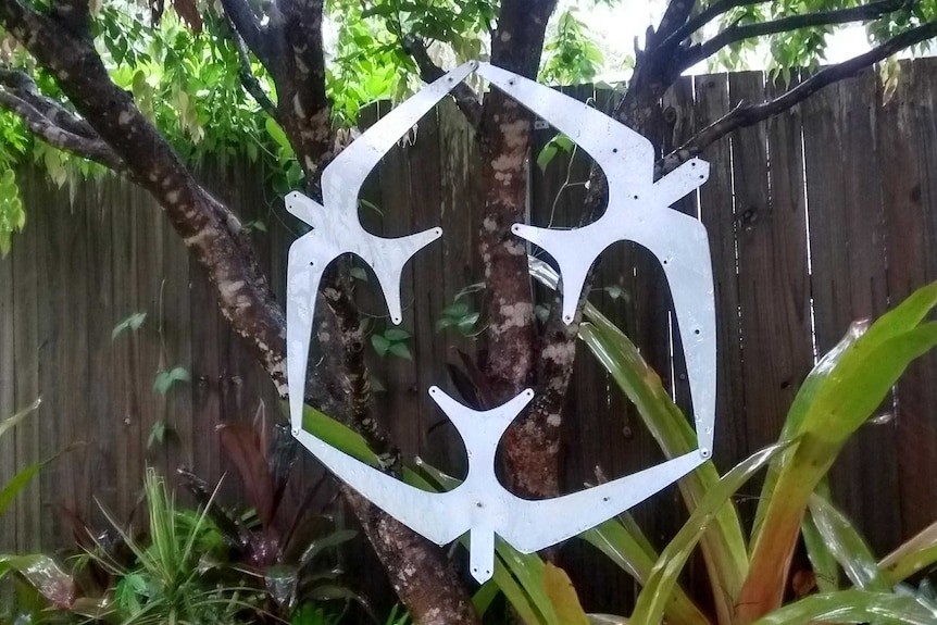 A metal mobile sculpture made of three metal birds linked together hangs off a tree in a back garden.