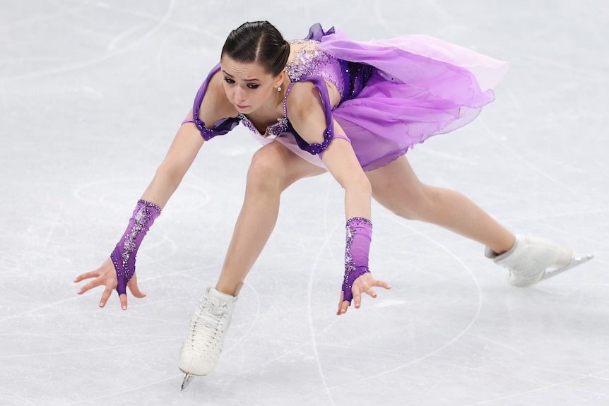 Kamila Valieva lands forward, her hands and arms out for balance.