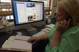 A blonde woman wearing a green top sits at a desk, talking on the phone.