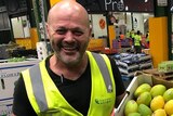 A man in high vis vest displays boxes of fruit and veg