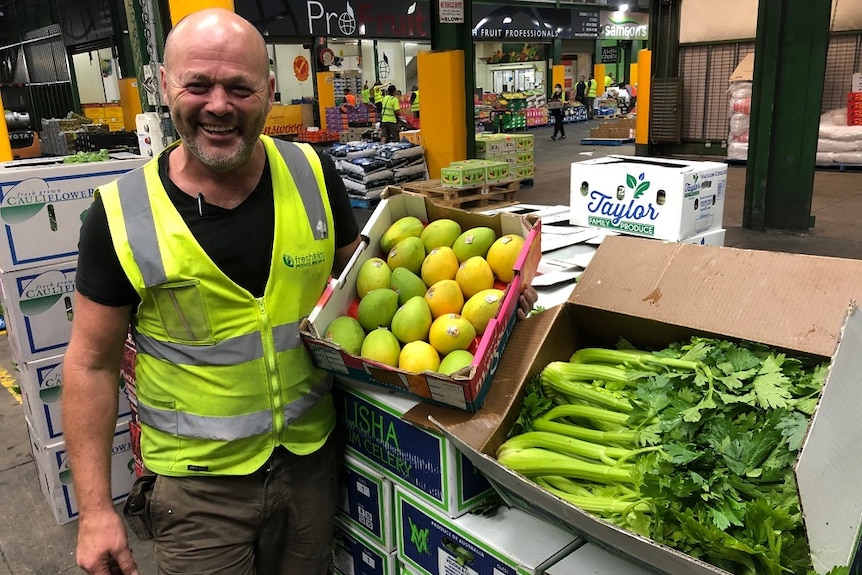 A man in high vis vest displays boxes of fruit and veg