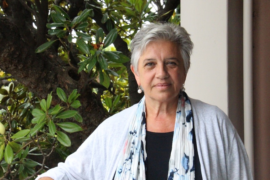 A woman with silver hair in front of a tree