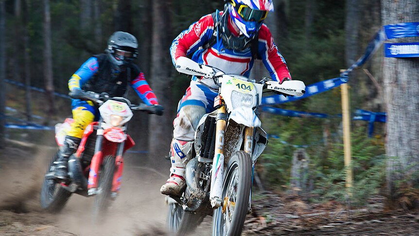 Two riders zip along a dirt track.
