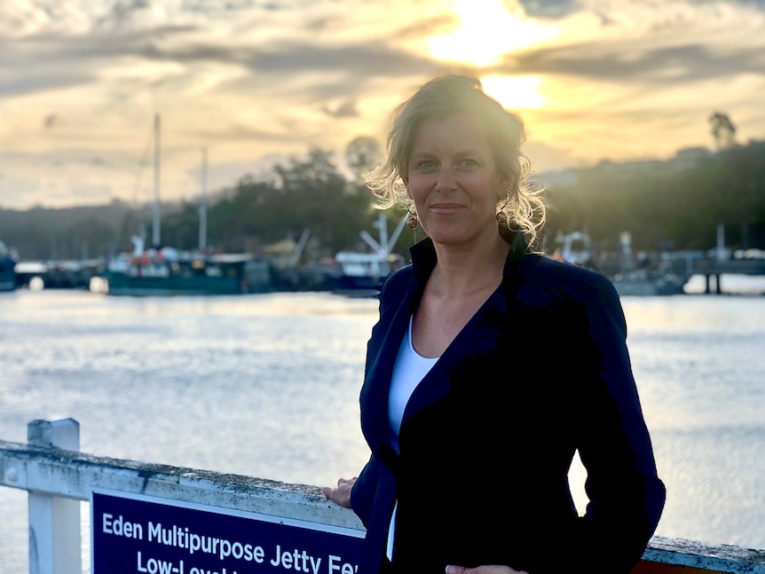 A woman in a business suit stands on a wharf with yachts in the background