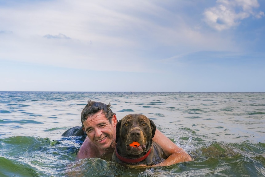 Aaron has an arm around his dog, as they swim