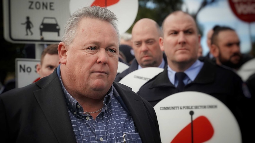 Tom Lynch stands in front of prison guards holding CPSU signs.