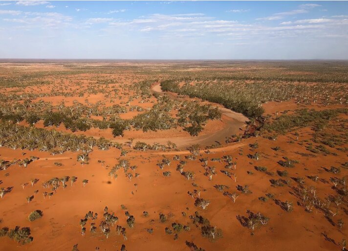 Uma fotografia de alto ângulo de terra vermelha e árvores ao longo de uma paisagem curva de um rio.