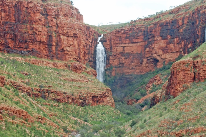 A waterfall flowing over red and green rocky gorge 