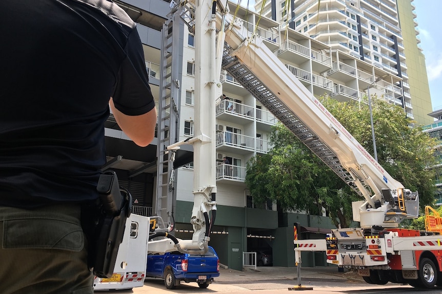 A fire truck ladder is raised outside a building where police are negotiating with a man on a balcony.