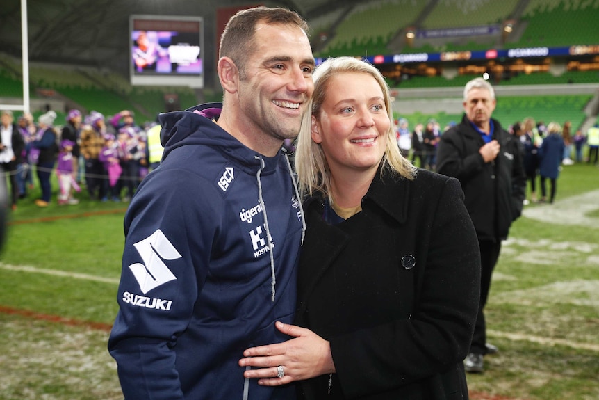A Melbourne Storm NRL players smiles as he and his wife pose for a photograph after a match.