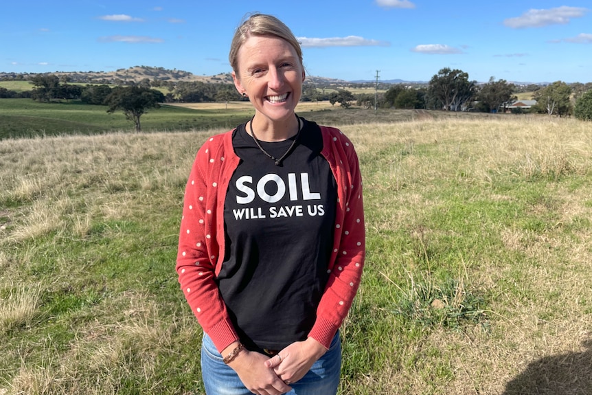 Una donna sorridente si trova di fronte a un campo di terra.