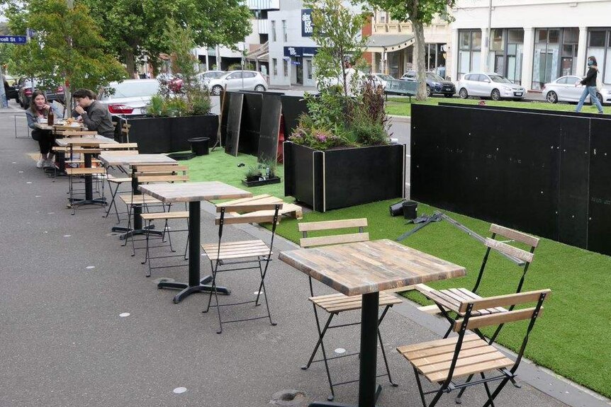 A row of distanced tables and chairs line the footpath outside a cafe in Melbourne.
