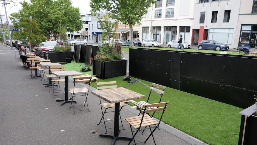 A row of distanced tables and chairs line the footpath outside a cafe in Melbourne.