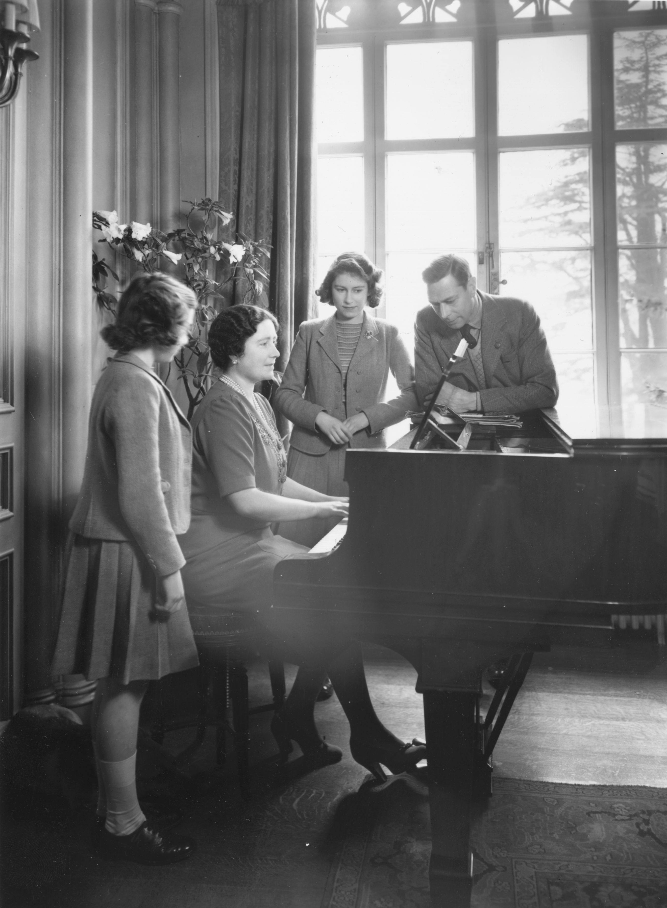 The young princesses Elizabeth and Margaret stand at a piano while their mother plays and King George VI looks on.