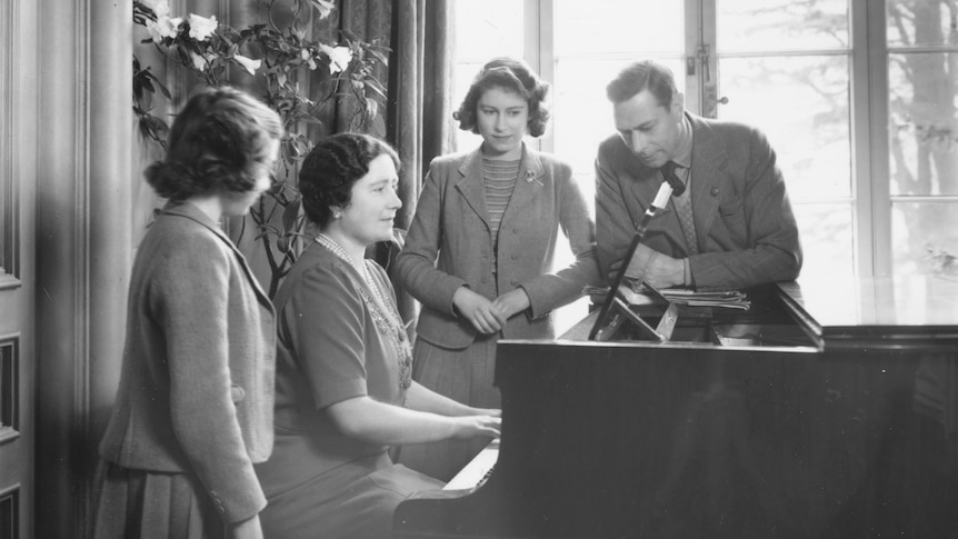 The young princesses Elizabeth and Margaret stand at a piano while their mother plays and King George VI looks on.