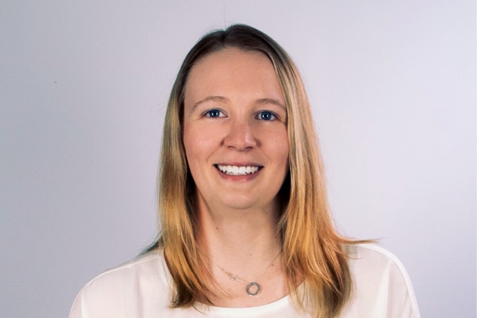 Kate Campbell smiles while standing against a white wall.