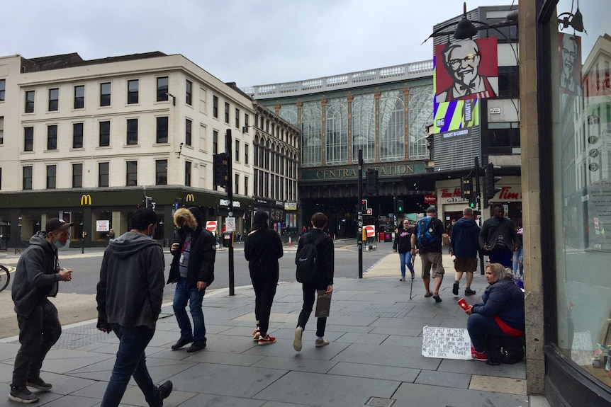 busy Glasgow street with homeless lady and sign