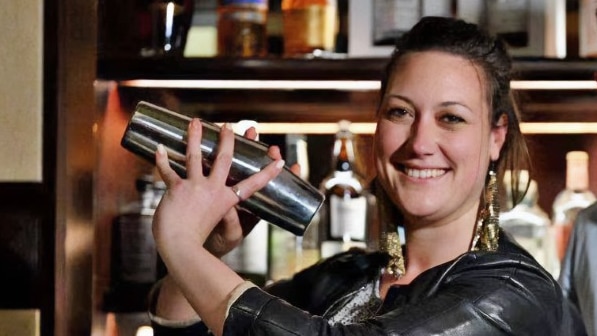 A woman with a cocktail shaker stands behind a bar with a man.