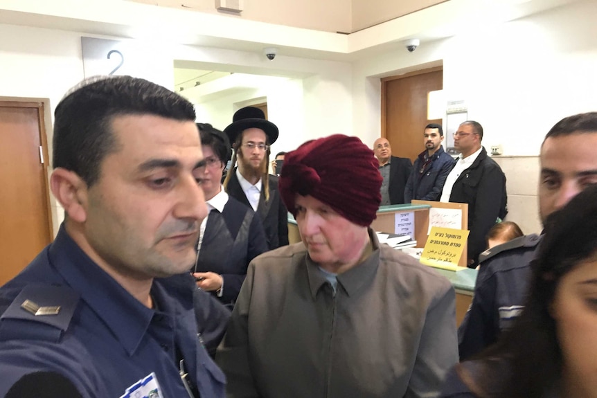 Malka Leifer sits in handcuffs guarded by police