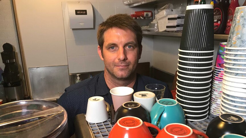 Darwin cafe owner Sam Weston stands behind coffee cups on top of a coffee machine.