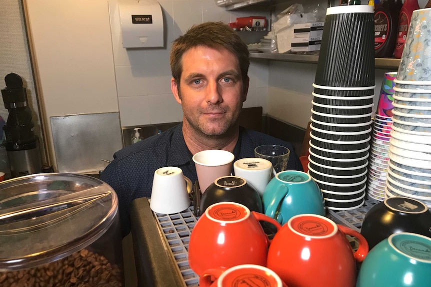 Darwin cafe owner Sam Weston stands behind coffee cups on top of a coffee machine.