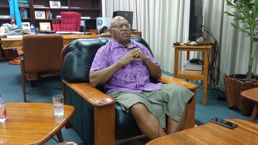 Sitiveni Rabuka sitting in a black leather lounge seat in an office. 