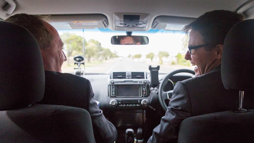 Barnaby Joyce, in the passenger's seat, smiles across at David Littleproud in the driver's seat. They are both wearing suits.