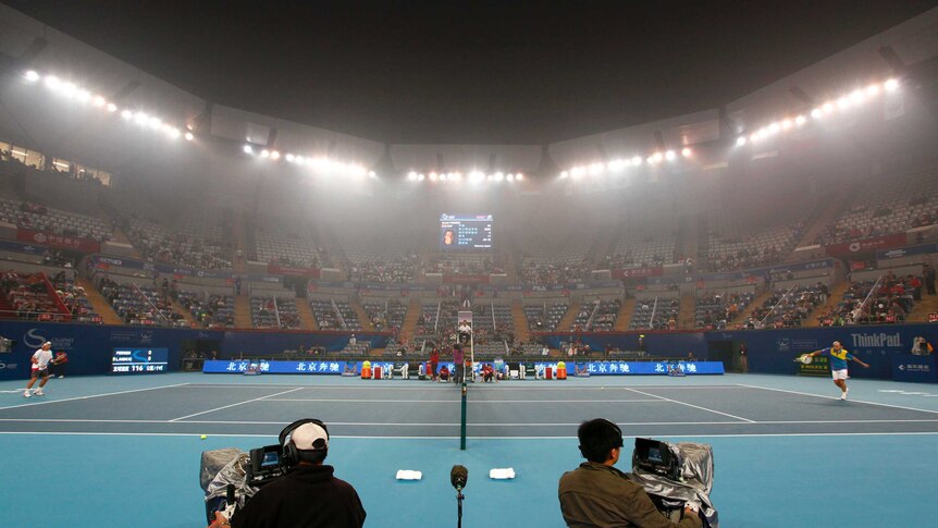 Players play a rally on a tennis court as smog lingers above near the flood lights