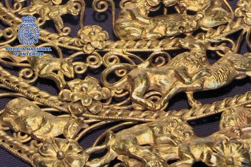 Primer plano de un collar de oro tallado con imágenes de caballos y flores.  