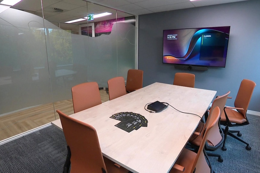 A meeting room with large table, chairs and a large wall mounted screen.