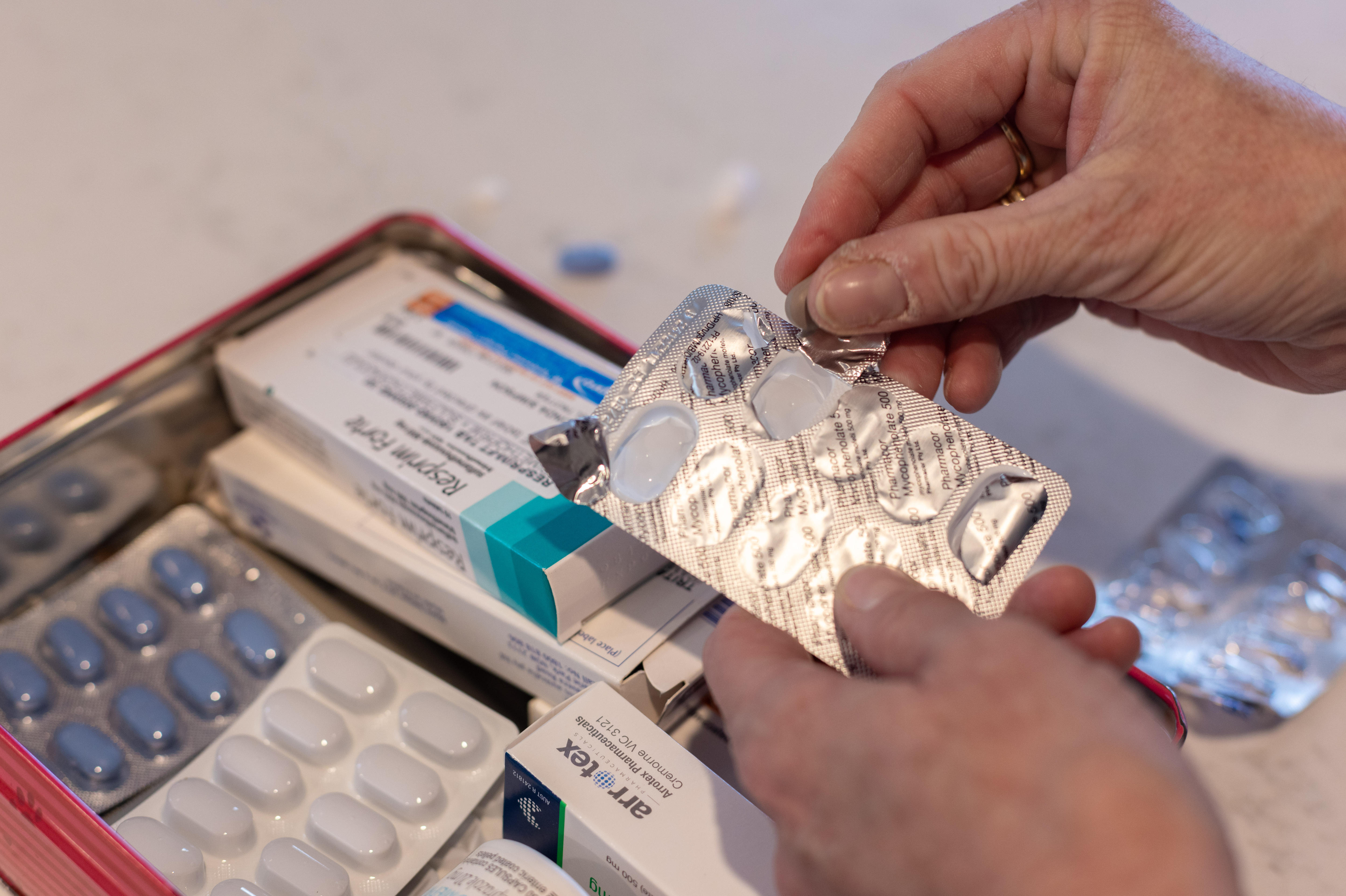 A photo of a hand holding a pill packet with a box of medications on the table