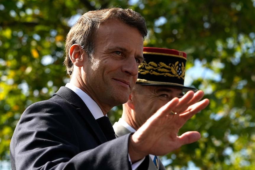 Emmanuel Macron is shown close up waving during the parade. 