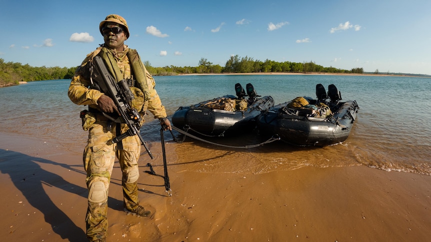 a man in army uniform on the beach pulling an inflatable boat to shore