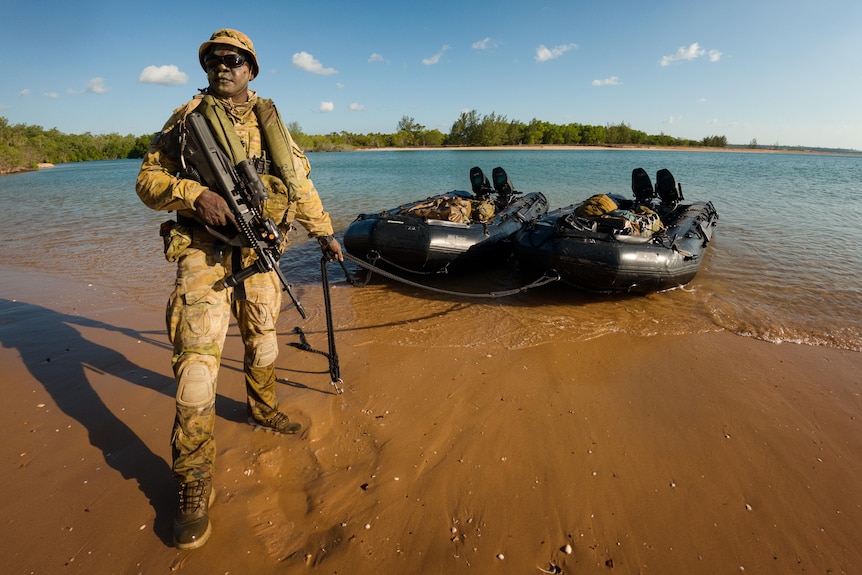 a man in army uniform on the beach pulling an inflatable boat to shore