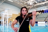 woman plays violin with indoor pool in background.