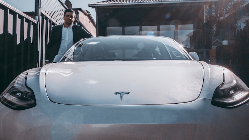 a man in a driveway with an electric car by tesla