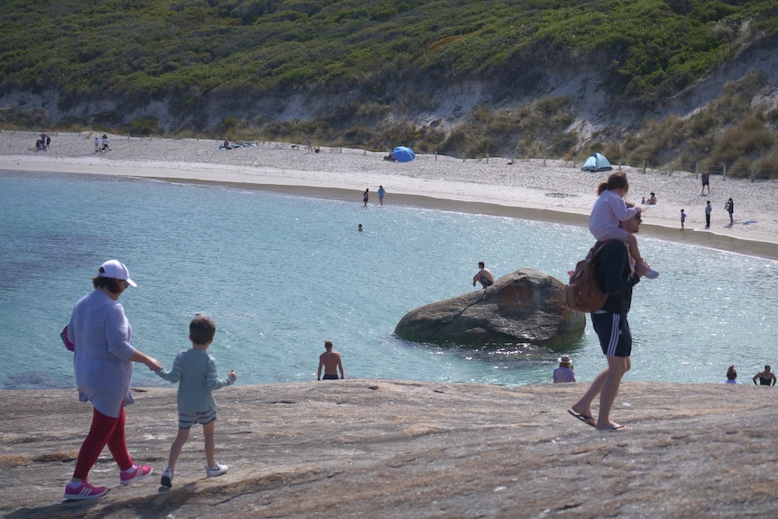 A family walking along rocks, next to a beach.