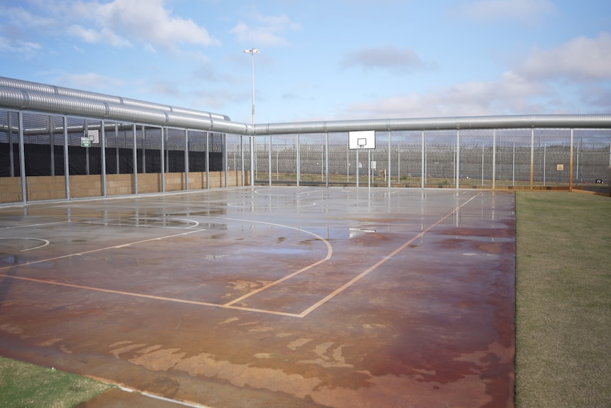 An outdoor basketball court on a cloudy day surrounded by a high fence
