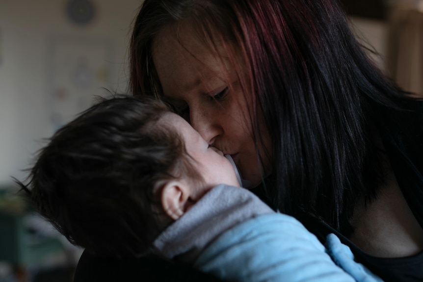 A woman leans in to kiss the few-months-old baby. The baby has thick brown hair.