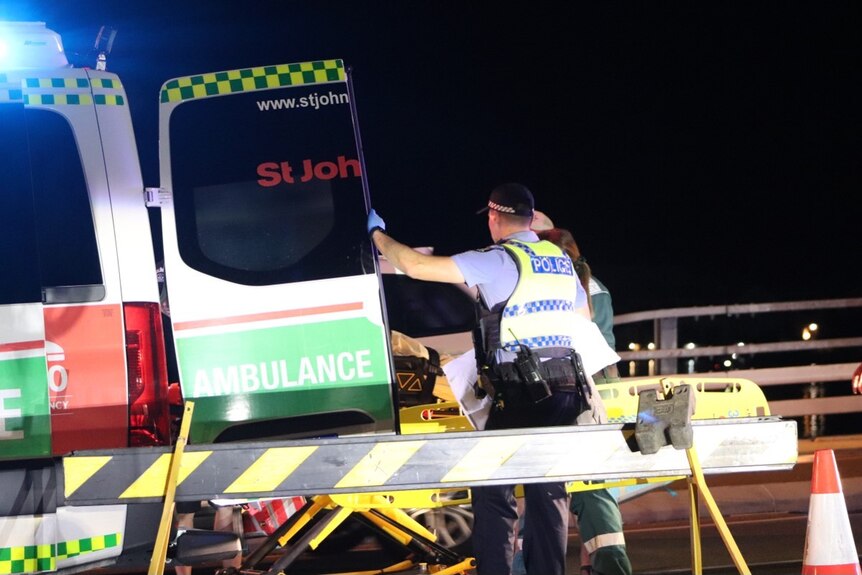 Police hold open ambulance door as someone is stretchered in 