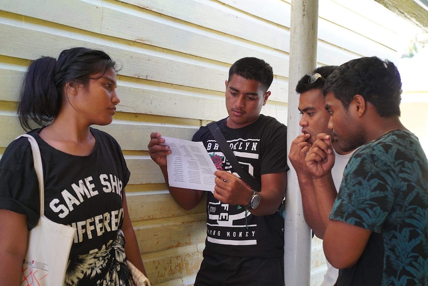 Four young people wearing t-shirts looking at piece of white paper and thinking. 