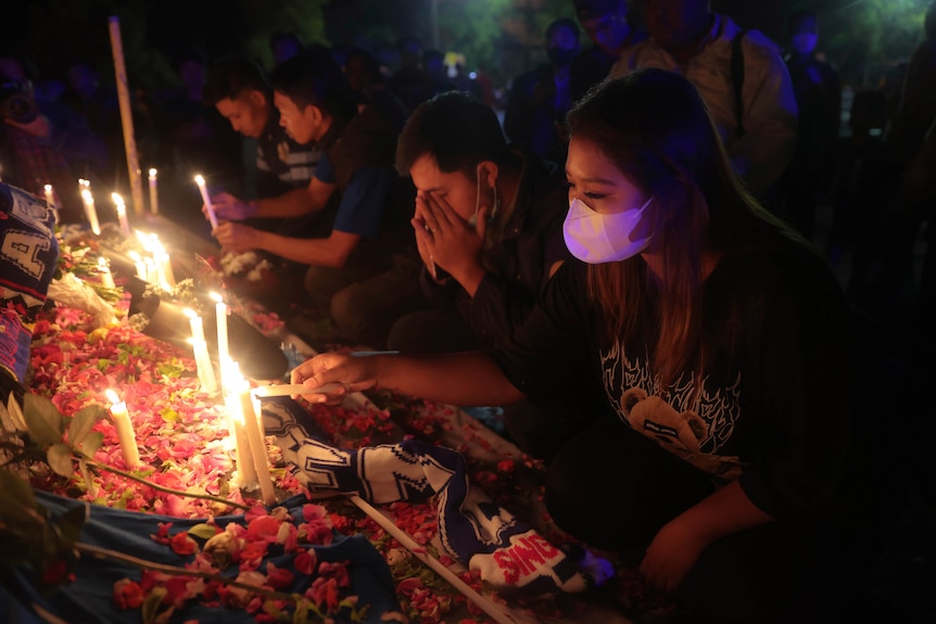 A woman lights a candle as a man prays beside her.