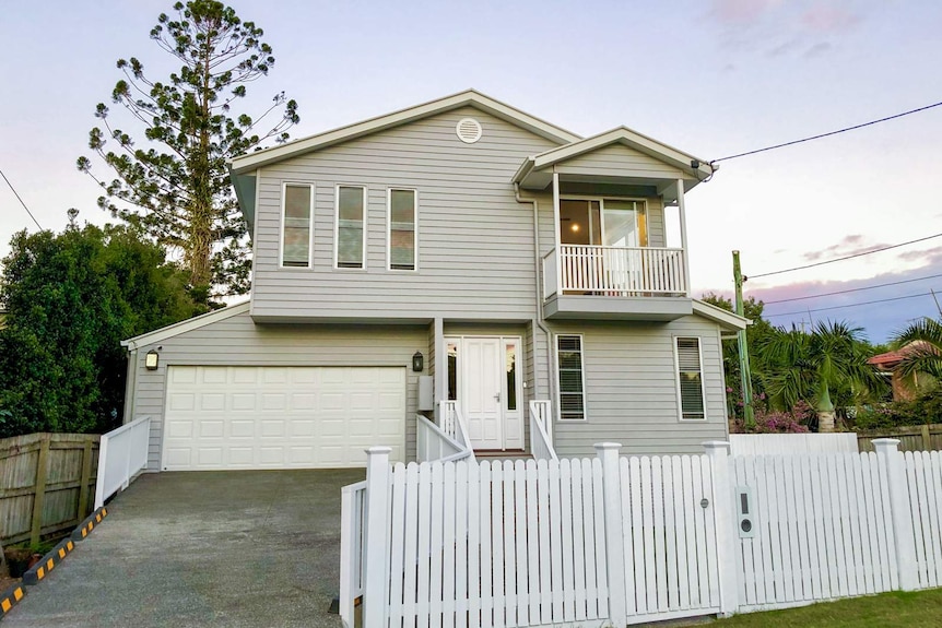 A two-storey grey house with a white fence.