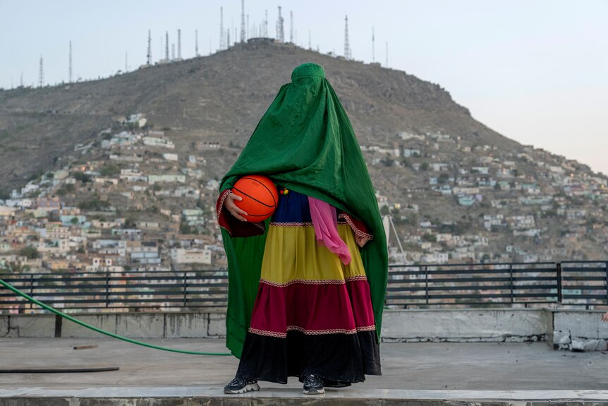 穿着绿色罩袍的阿富汗妇女拿着篮球站着。