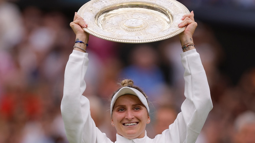 Marketa Vondrousova holds up a plate-shaped golden trophy and smiles