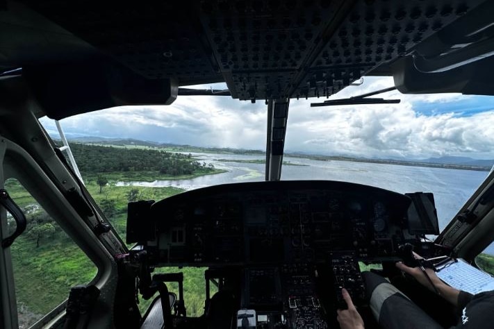 Looking over the shoulder of a helicopter pilot as the pilot flies over a body of water.